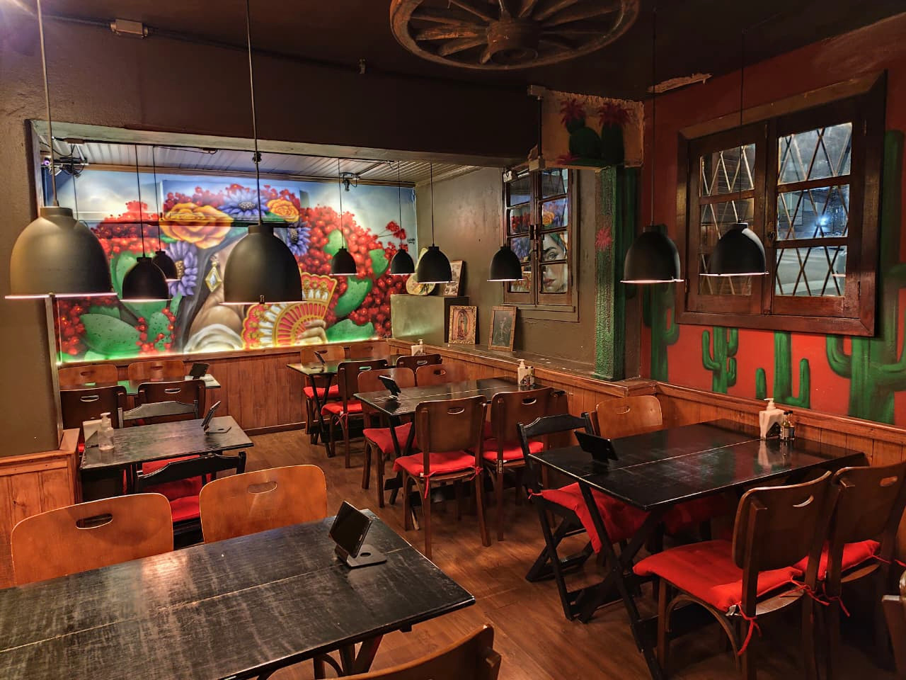 Salão com luminárias, mesas e mural mexicano